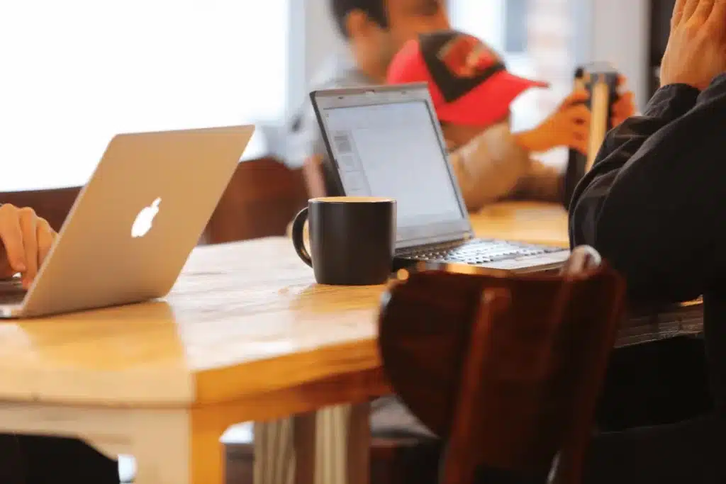 Freelancer typing on a MacBook in a cozy coffee shop environment.
