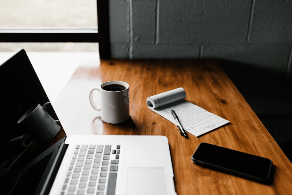 Modern workspace with a laptop, coffee mug, and notepad on a wooden table.