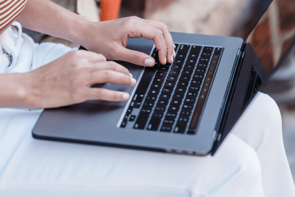 Close-up of hands typing on a laptop while seated outdoors.