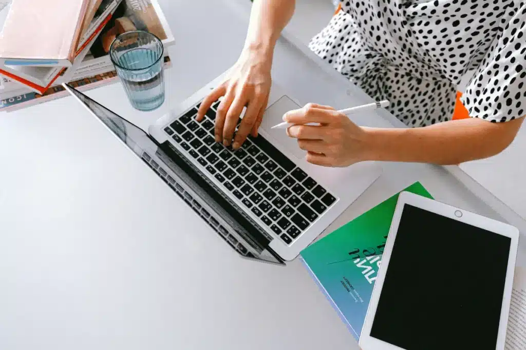 Creative workspace with a laptop, digital tablet, glass of water, and books on a modern white desk.
