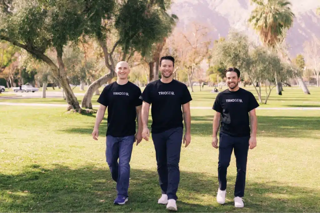 Smiling Nathan, Steven, and Connor walking in a lush green park on a clear day.