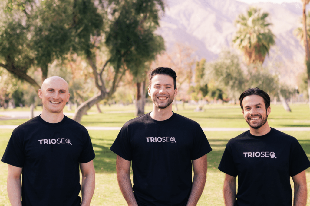 Nathan, Steven, and Connor in TrioSEO shirts smiling in a park with mountains in the background.