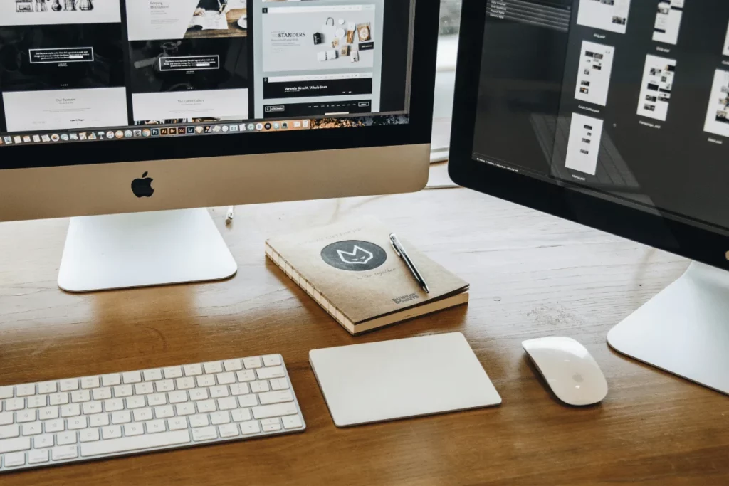 A neatly organized designer workspace with two Apple iMacs and various design materials.