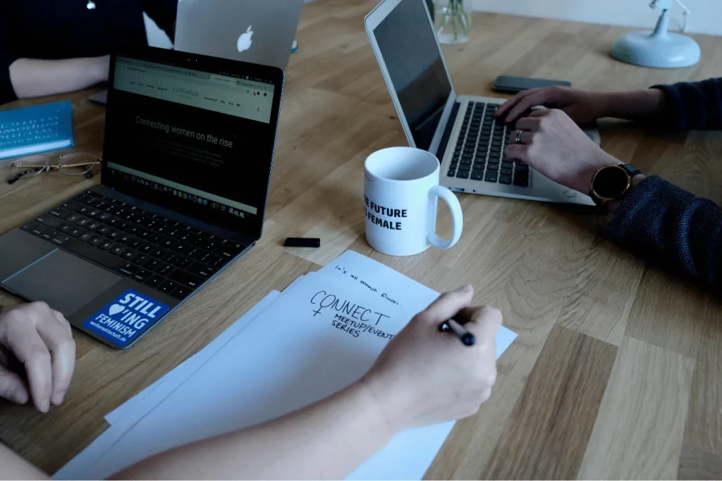 Business professionals at a wooden table with laptops, discussing strategies, highlighting women empowerment themes.