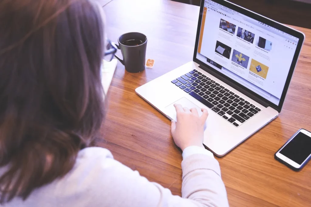 Woman browsing content marketing strategies on a MacBook at a wooden desk with coffee.