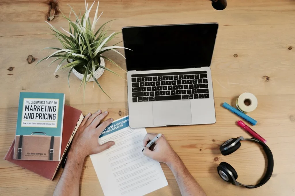 Overhead view of a workspace with a laptop, marketing books, and office supplies.