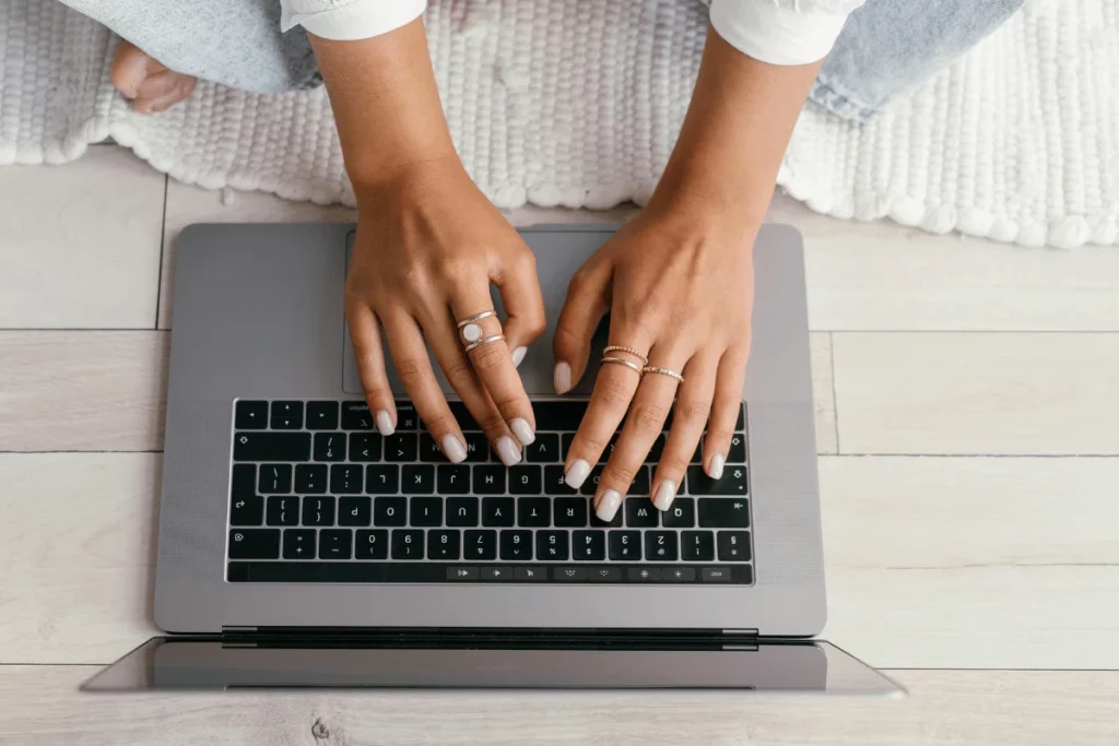 Elegant hands with rings using a MacBook on a wooden floor.