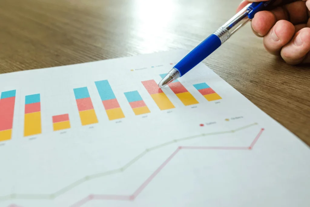 Close-up of a hand holding a pen, analyzing a colorful bar chart on a paper.