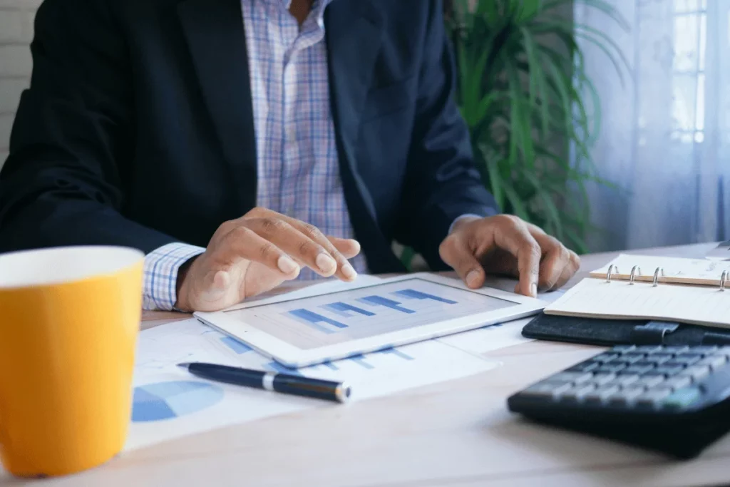 Man in a suit reviewing charts on a tablet at a desk.
