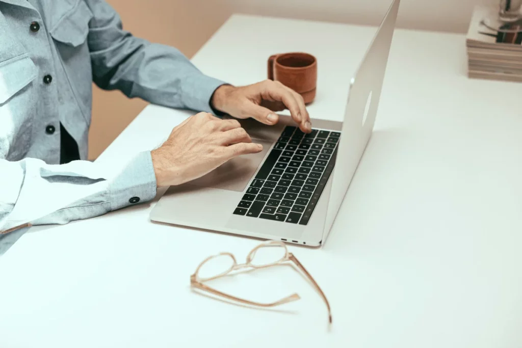 Person working on a MacBook with glasses and a cup nearby.