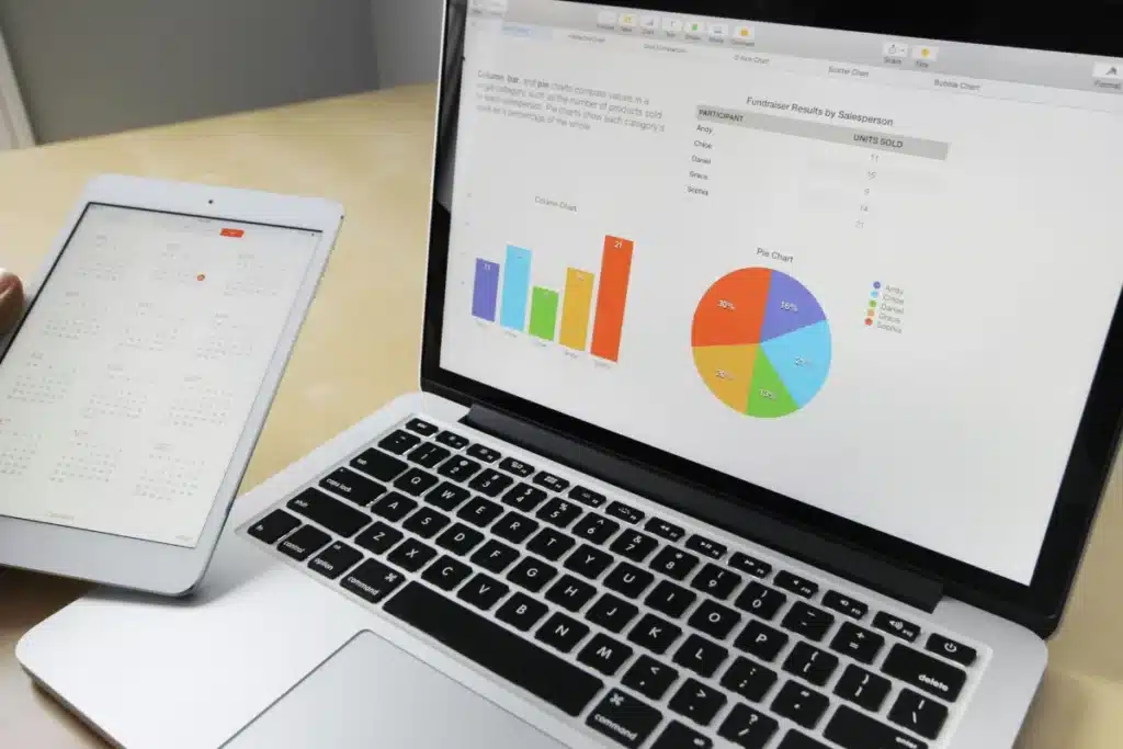 Close-up of a laptop and tablet displaying charts and a calendar on a wooden table, highlighting data analysis tools.